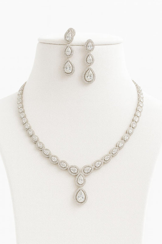 Bellissima Glow necklace set with teardrop CZ stones in white plating, paired with matching earrings, displayed on velvet and bust stand