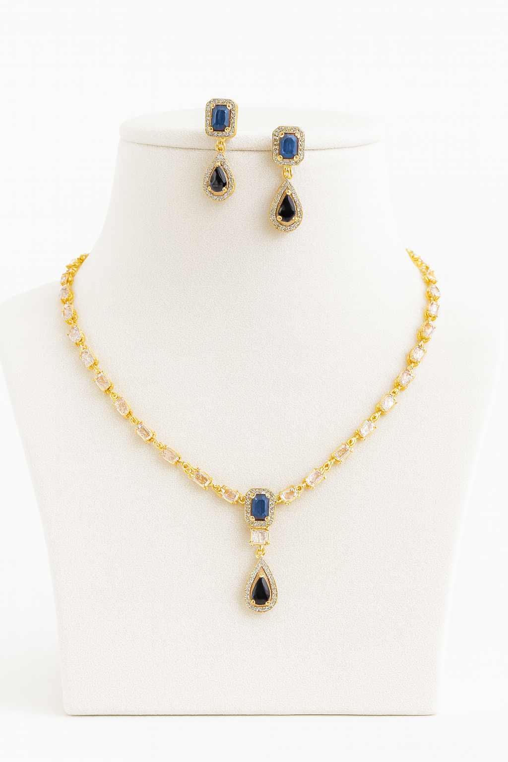 Aria Finezza necklace set displayed on a grey bust, featuring blue rectangular and teardrop stones with gold CZ detailing