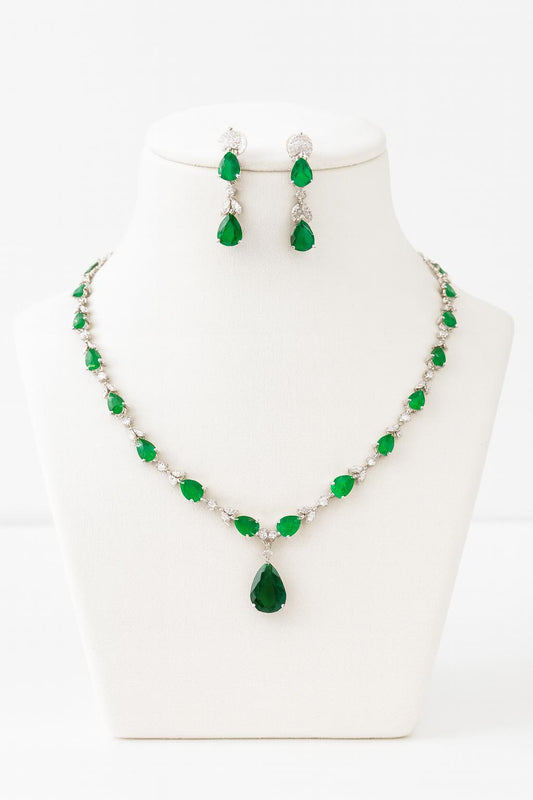 : “Luna Milano delicate CZ necklace set on a velvet bust, featuring green teardrop stones with white plating.”