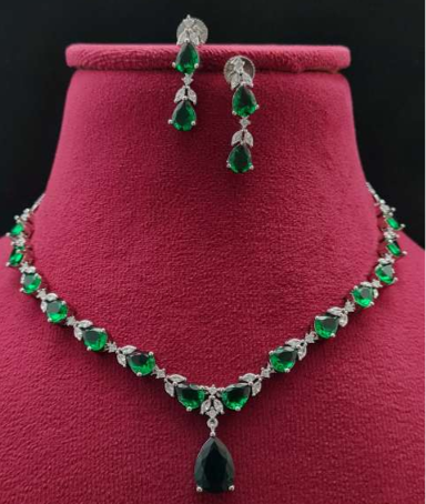 : “Luna Milano delicate CZ necklace set on a velvet bust, featuring green teardrop stones with white plating.”
