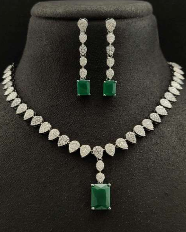 Jewelry set with necklace and earrings featuring green gemstones on a black stand.