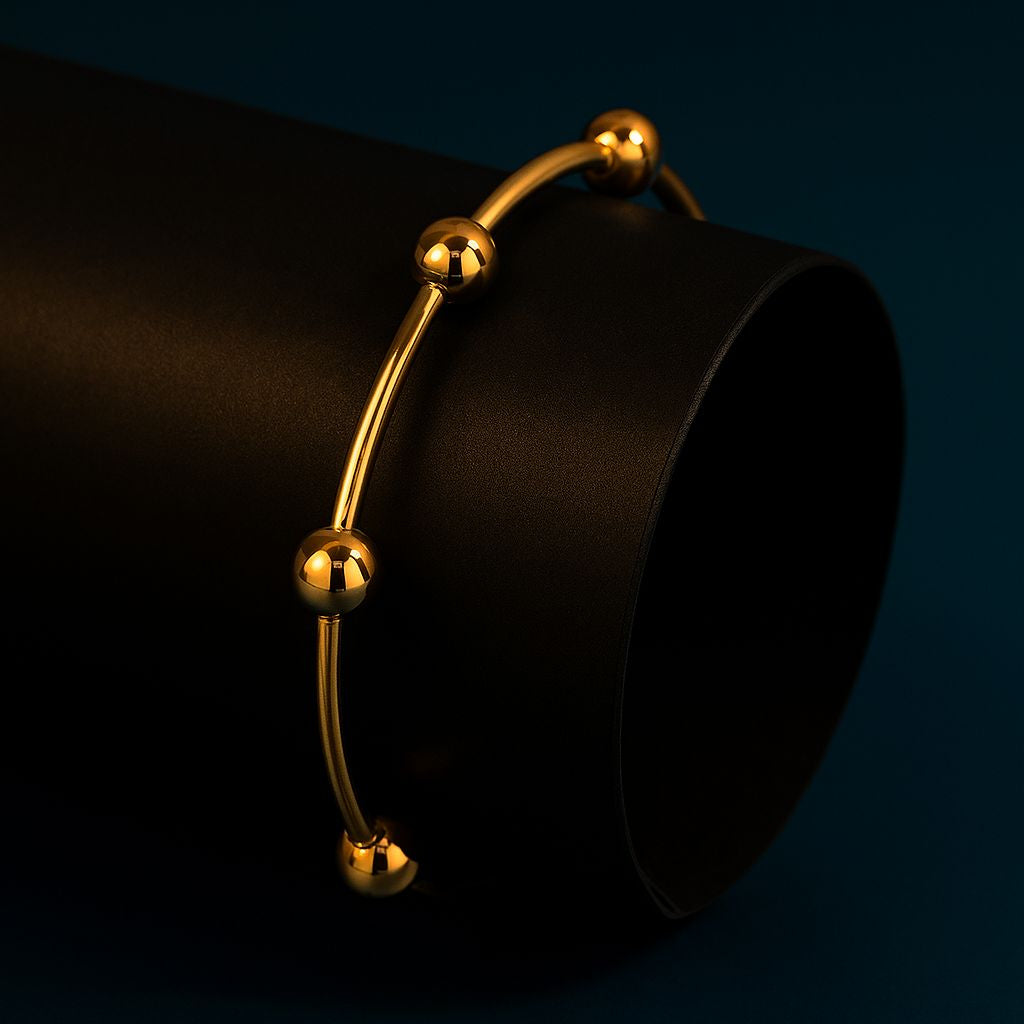 Gold bracelet on a black cylindrical object against a dark background