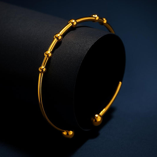 Gold bracelet on a black cylindrical object against a dark blue background