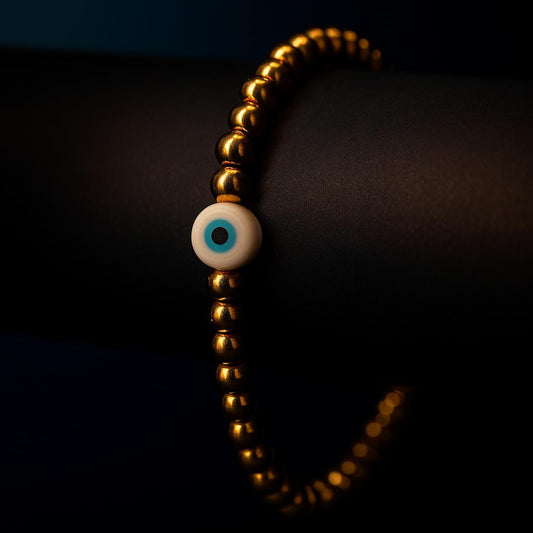 Gold beaded bracelet with a central evil eye charm on a dark background