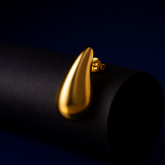 Rayne Stud Gold Earrings displayed on black matte surface against deep blue background, minimalist teardrop design