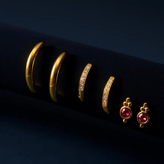 Gold hoop earrings and pink gemstone earrings on a dark background
