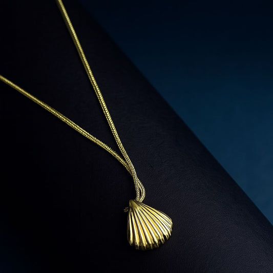 "Aura Shell Pendant Necklace in 18K PVD gold plated stainless steel on dark textured surface with navy background"