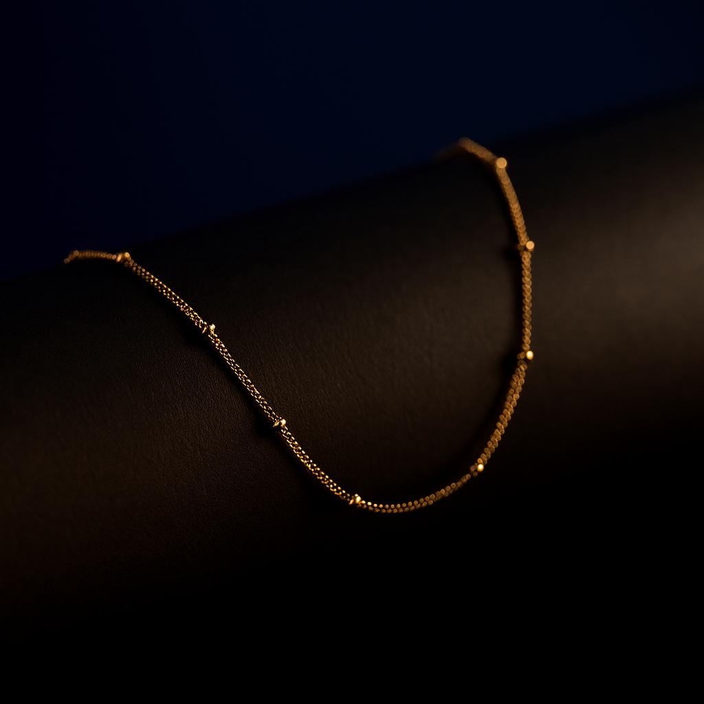 "Oceanic Glow Beaded Chain Necklace in 18K PVD gold plated stainless steel on dark cylindrical surface with navy background"