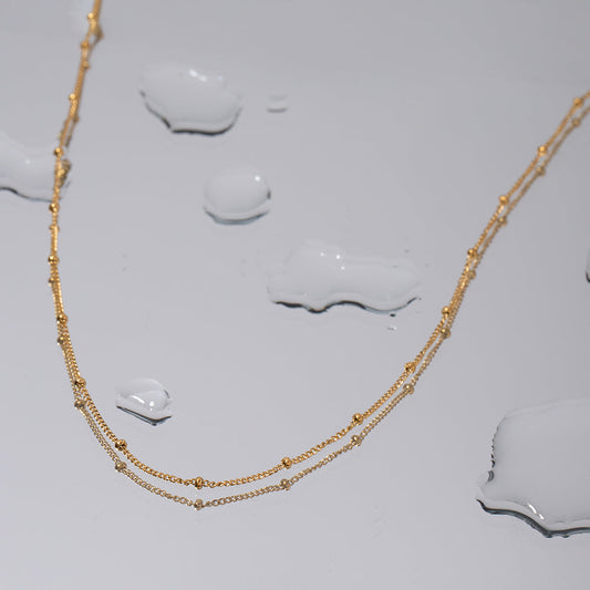 "Oceanic Glow Beaded Chain Necklace in 18K PVD gold plated stainless steel with water droplets on reflective surface"
