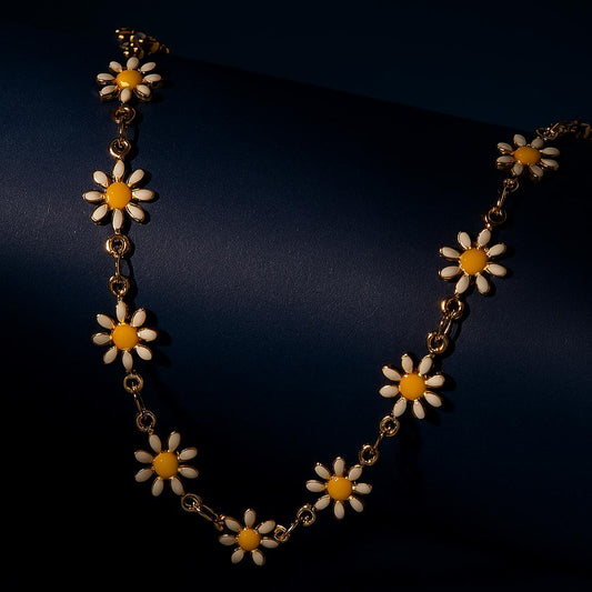 "Solara Daisy Charm Necklace with enamel flowers in 18K PVD gold plated stainless steel on dark cylindrical surface with navy background"