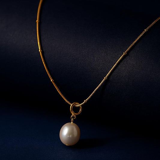 "Gilden Necklace with natural freshwater pearl pendant on bead-accented chain in 18K PVD gold plated stainless steel on dark cylindrical surface with navy background"