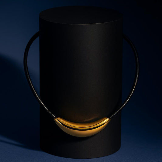 FIORENZA Gold Necklace with curved gold centrepiece on black cord – dark display backgroundbackground