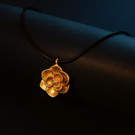 LUMINA Gold Necklace with camellia flower pendant on black cord – dark display backgroundbackground