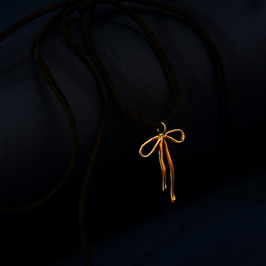 SAVINA Gold Necklace with bow pendant on black rope – dark display background
