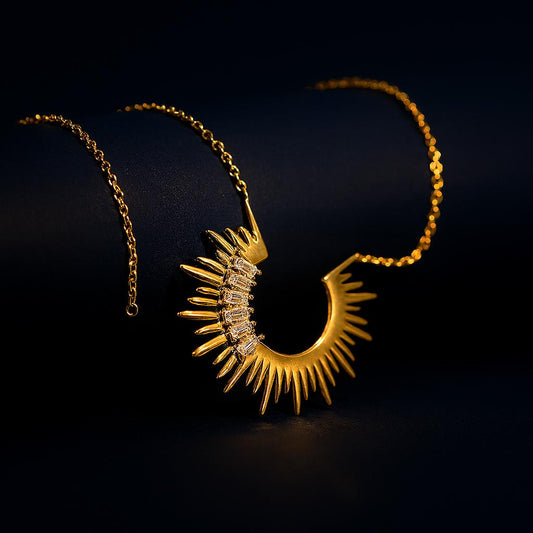 Sunkissed Gold Necklace on dark surface – close-up of gold sun charm with rectangular zircon stones.