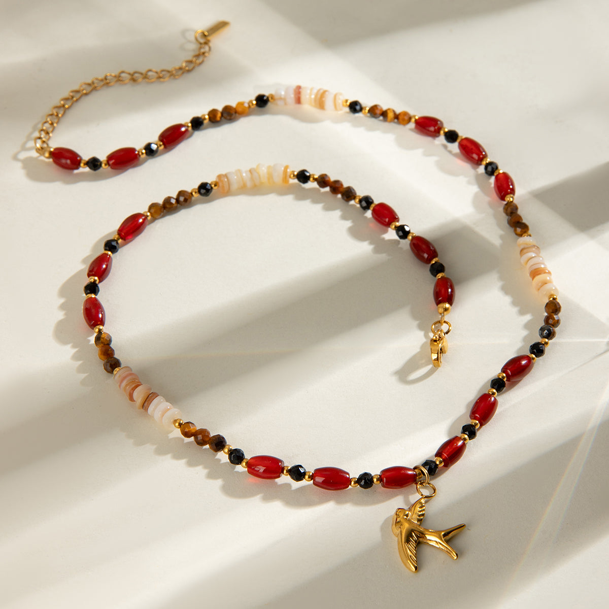 Onyx Gold Necklace with natural stones, crystals, and gold bird pendant – flat lay