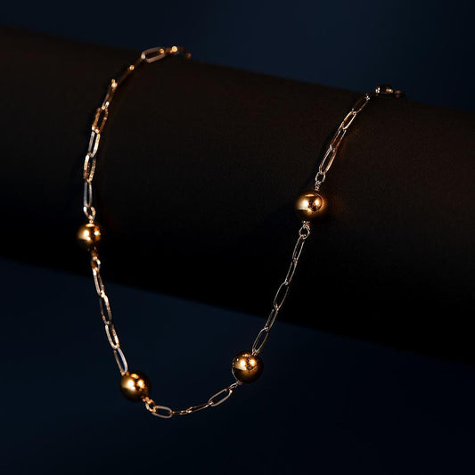 Minimalist silver chain with gold beads, displayed on dark cylindrical surface.