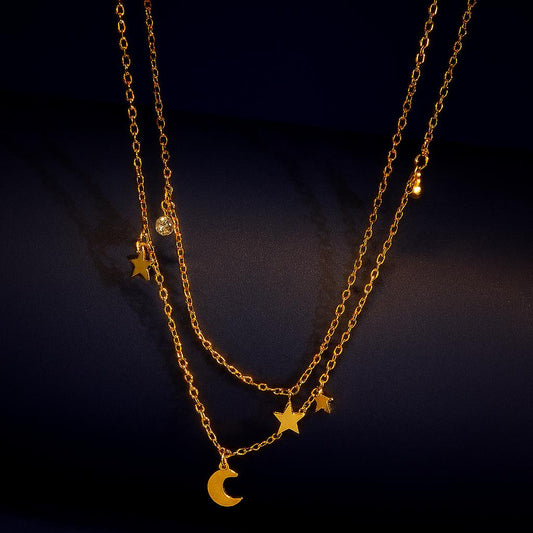 Kismet Gold Double Layer Necklace with star, moon & crystal charms on a dark backgroundbackground