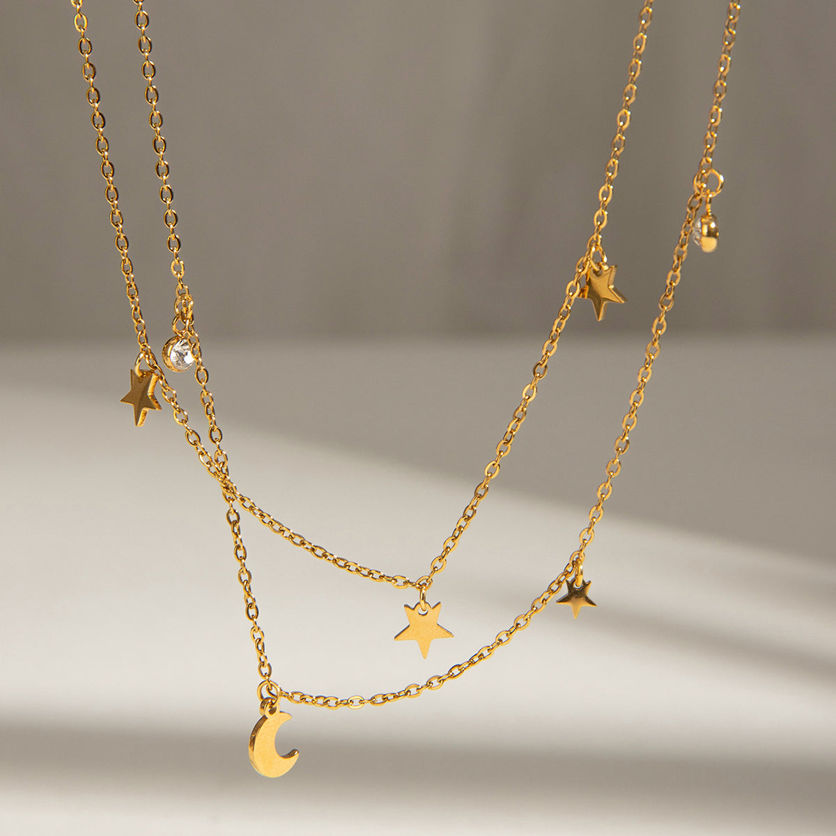 Kismet Gold Double Layer Necklace with star, moon & crystal charms on a light background