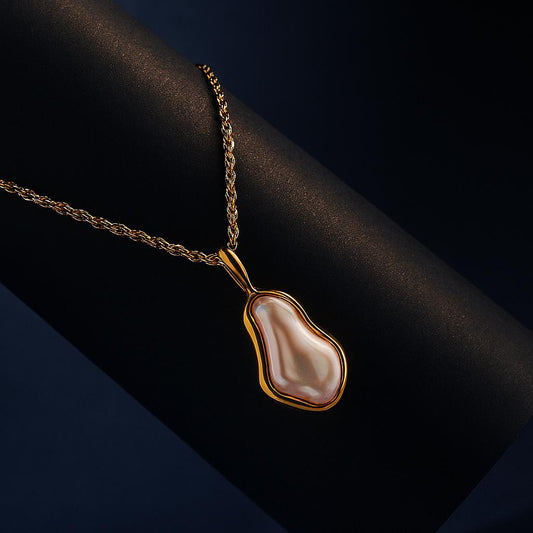 Sierra Gold Necklace – organic pearl pendant displayed on gold chain over black matte roll with navy backdrop

