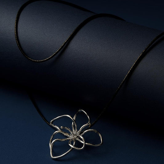 Quinn Silver Necklace – silver wire flower pendant displayed on black cord over navy matte roll backdropbackground