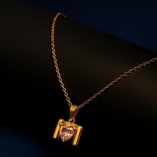 Gold necklace with a heart-shaped pink gemstone pendant on a dark background