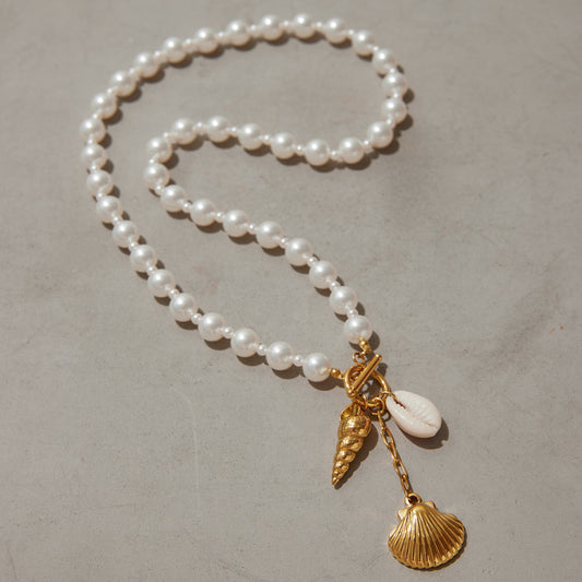 Jade Gold Necklace – pearl chain with gold and natural seashell charms on stone background