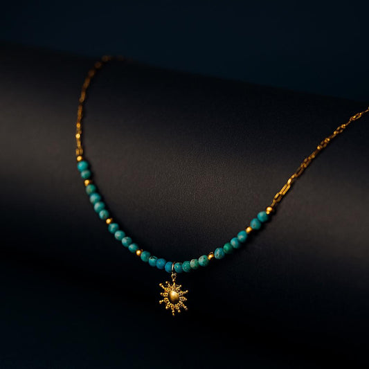 Gala Gold Necklace – turquoise beads and gold sun charm displayed on black matte roll with navy backdropbackground