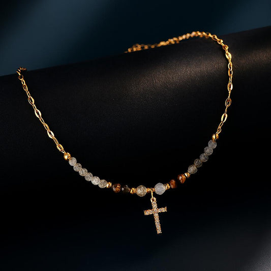 Lyric Gold Necklace – gemstone beads and zirconia cross pendant displayed on gold chain over black matte roll with navy backdrop