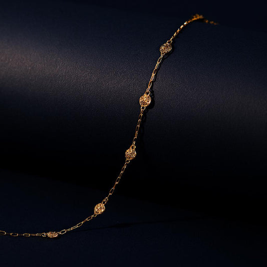 Elysian Gold Necklace – textured gold charms along chain displayed over black matte roll with navy backdrop