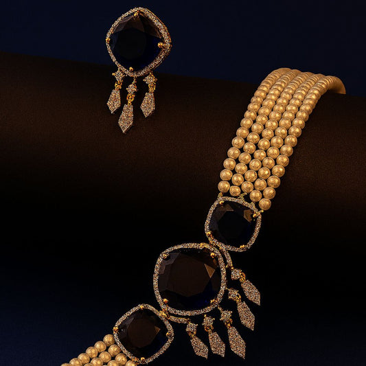 Gold necklace with black stones and matching earrings on a dark background